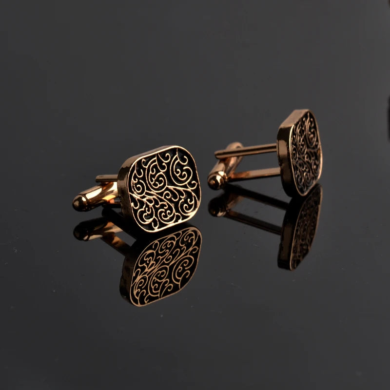 Pair of gold cufflinks with intricate design on a black reflective surface