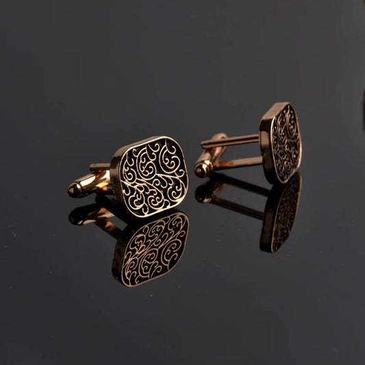 Pair of gold cufflinks with intricate design on a black reflective surface